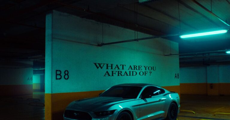 A Ford Mustang parked in a dimly lit garage with 'What are you afraid of?' on the wall.