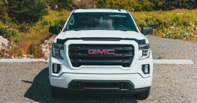 Front view of a white GMC truck parked on a scenic road with trees in the background.