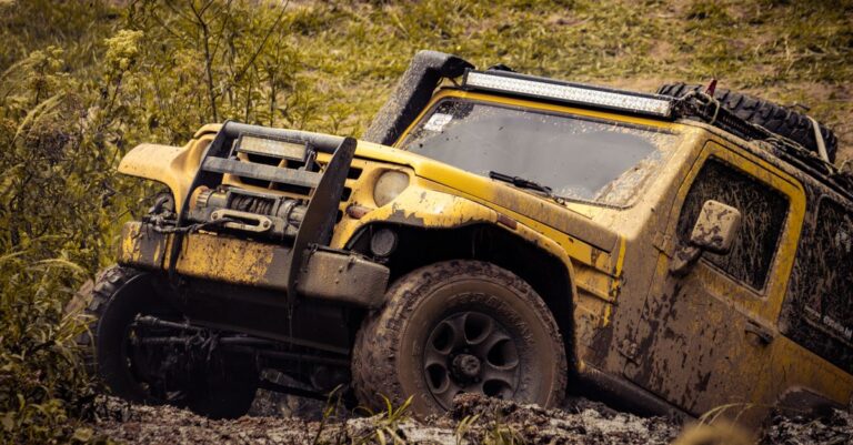 Yellow 4x4 SUV tackling a muddy off-road path in a rugged outdoor setting.
