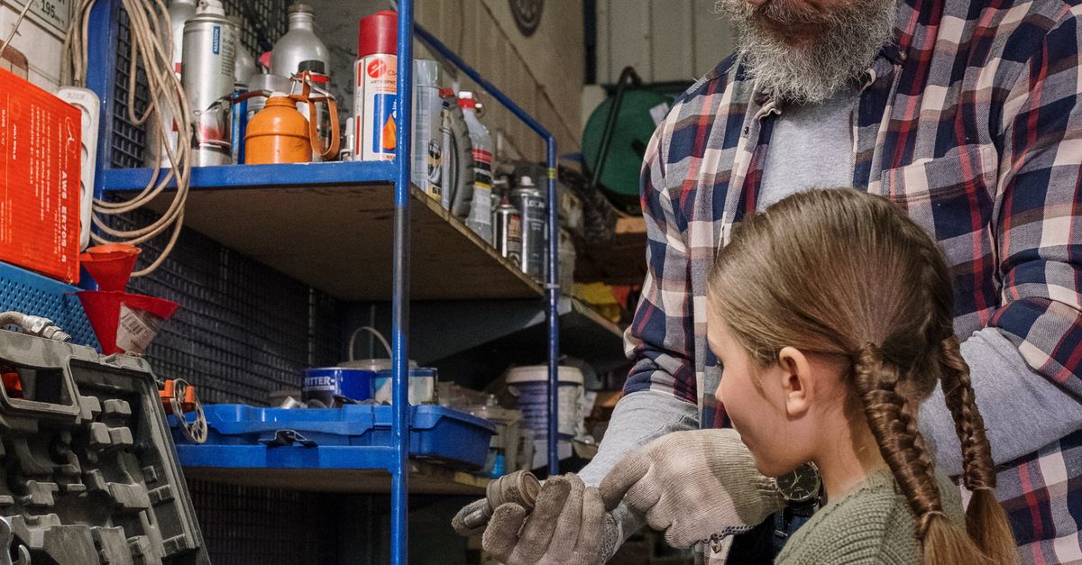 Dad teaching daughter car mechanics in a garage, emphasizing family bonding and practical skills.