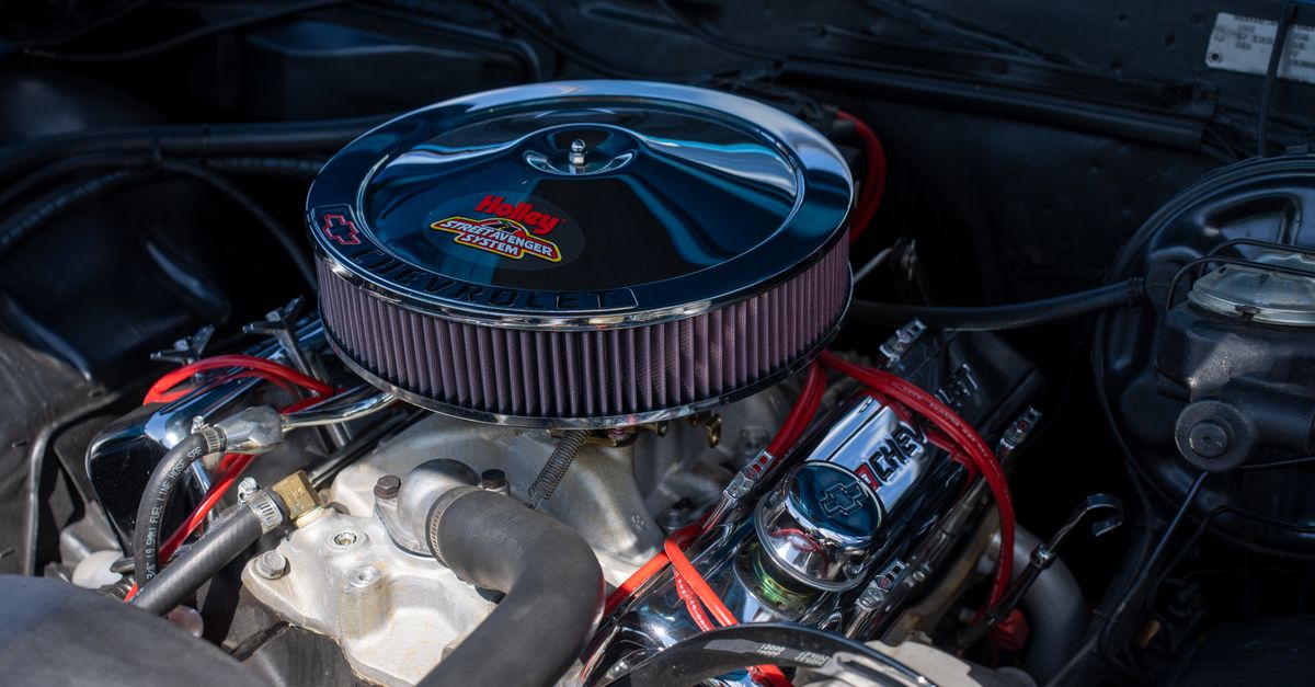 Detailed view of a classic car engine featuring a shiny Holley air filter and red ignition wires.