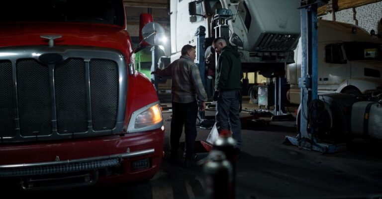 Mechanics performing truck maintenance and repair in an indoor garage setting.
