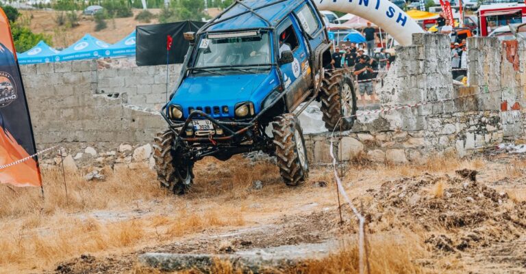 Blue off-road vehicle tackles rugged terrain at a competitive event.