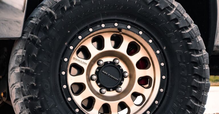Detailed view of an off-road tire with rugged tread on a vehicle parked on gravel.