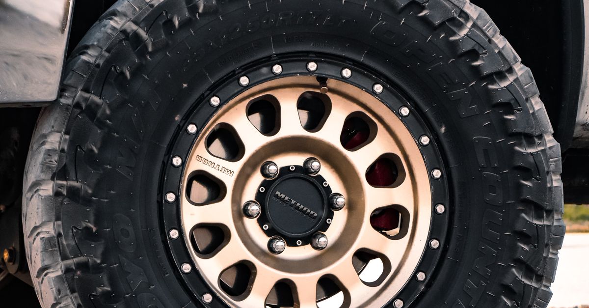 Detailed view of an off-road tire with rugged tread on a vehicle parked on gravel.