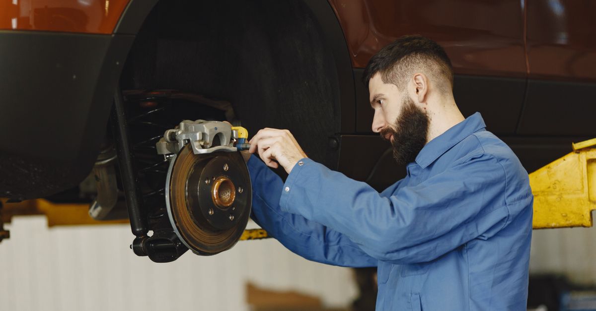 Mechanic in blue uniform performing brake repair on car in modern garage.