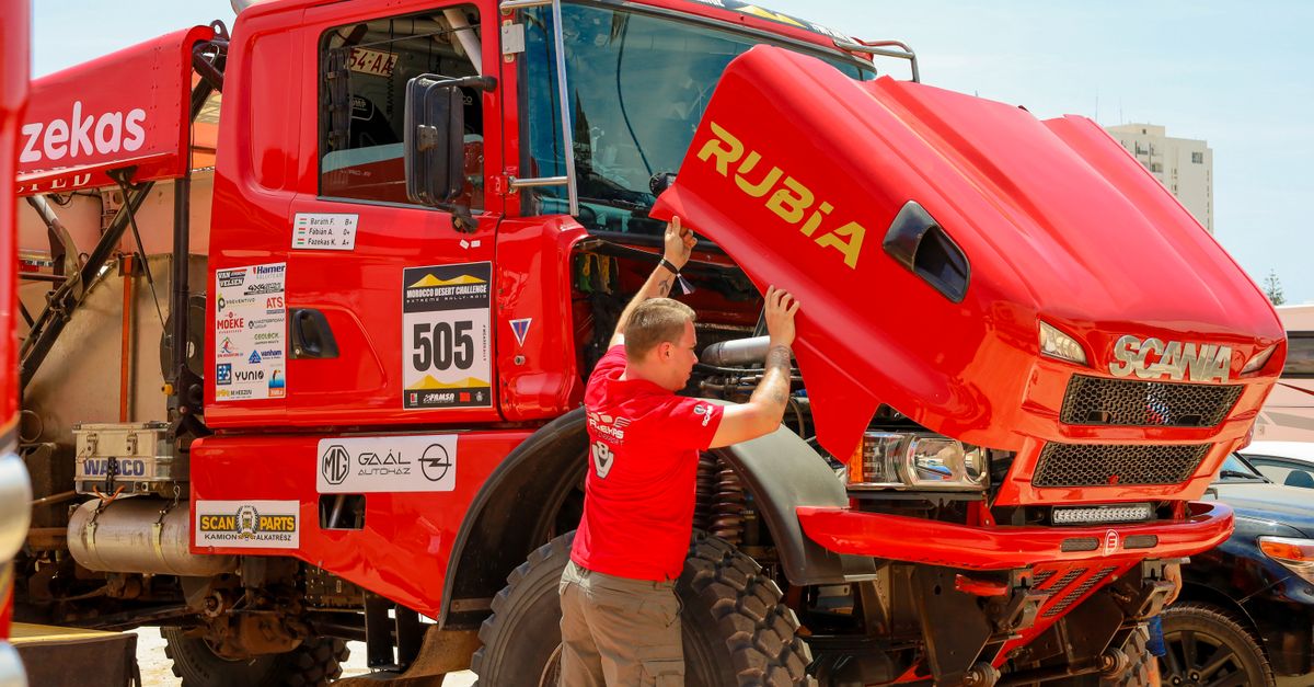 Mechanic checking a red rally truck's engine during a desert competition event.