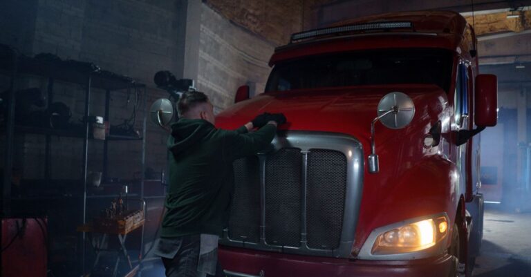 A mechanic in a dimly lit garage working on a red semi truck, focus on repair.