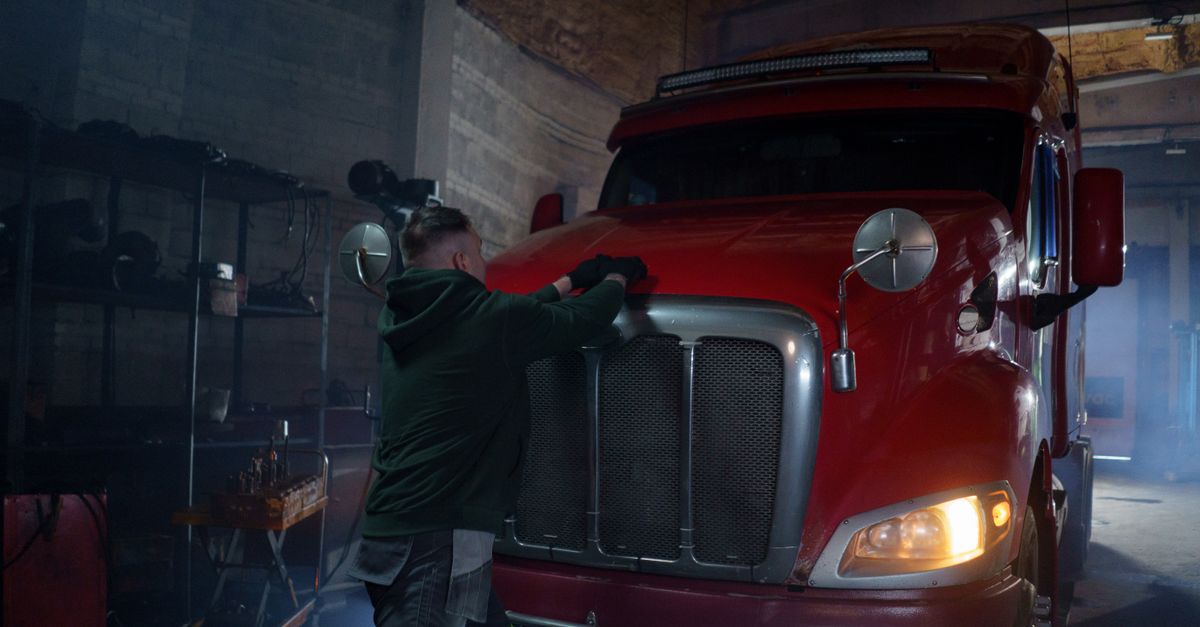 A mechanic in a dimly lit garage working on a red semi truck, focus on repair.