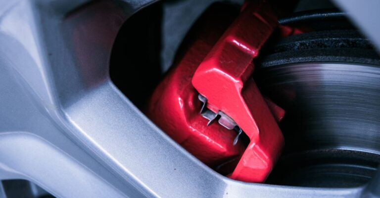 Detailed photo of a red automotive brake caliper and disc brake in focus.