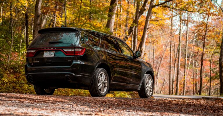 A sleek black SUV parked on a gravel road surrounded by autumn foliage, exuding a sense of adventure.
